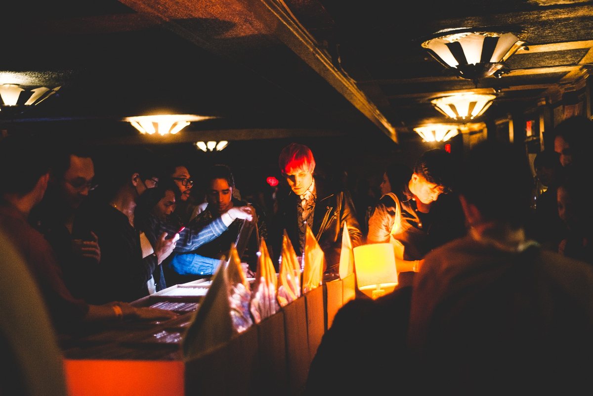 Crate-digging at a We Share Records stall: people flipping through records at a counter under warm lamps in a dark room