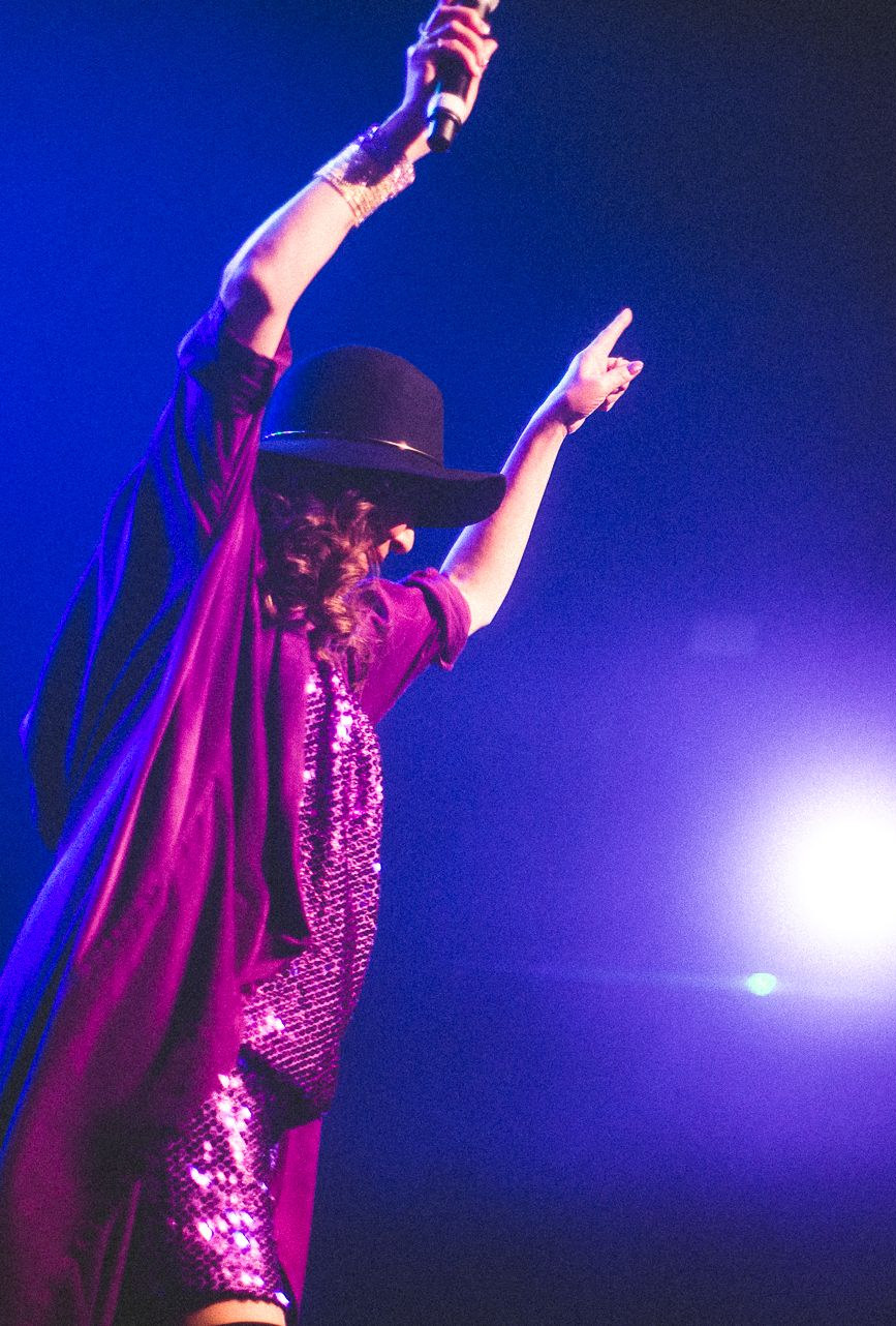 A performer raising both arms on stage, lit blue, at a past event